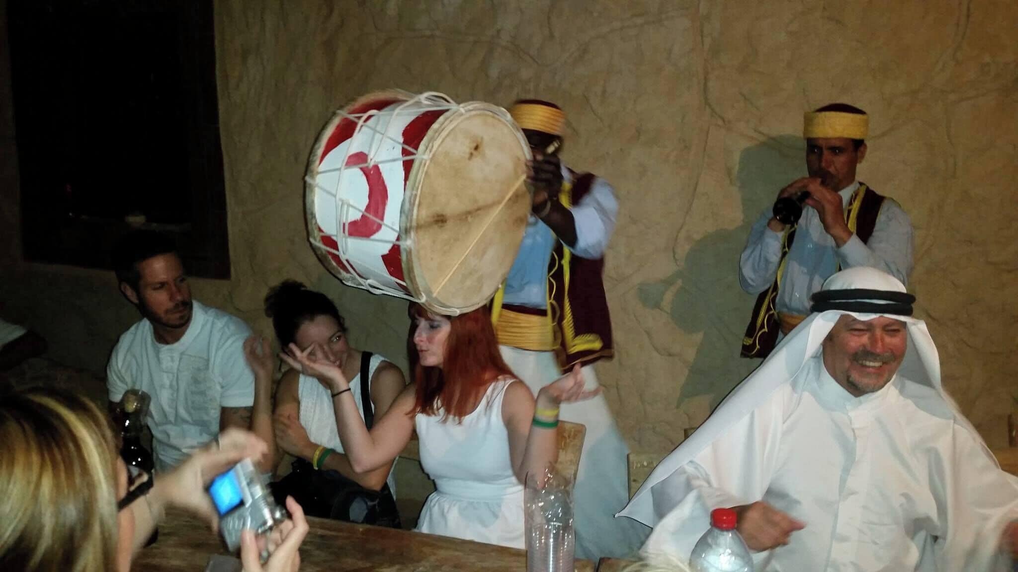 Un grupo de personas, algunas vestidas con atuendos tradicionales, reunidas alrededor de una mesa con un tambor.