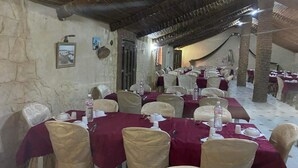 Un restaurante con mesas dispuestas para comer, paredes de piedra y un techo rústico.