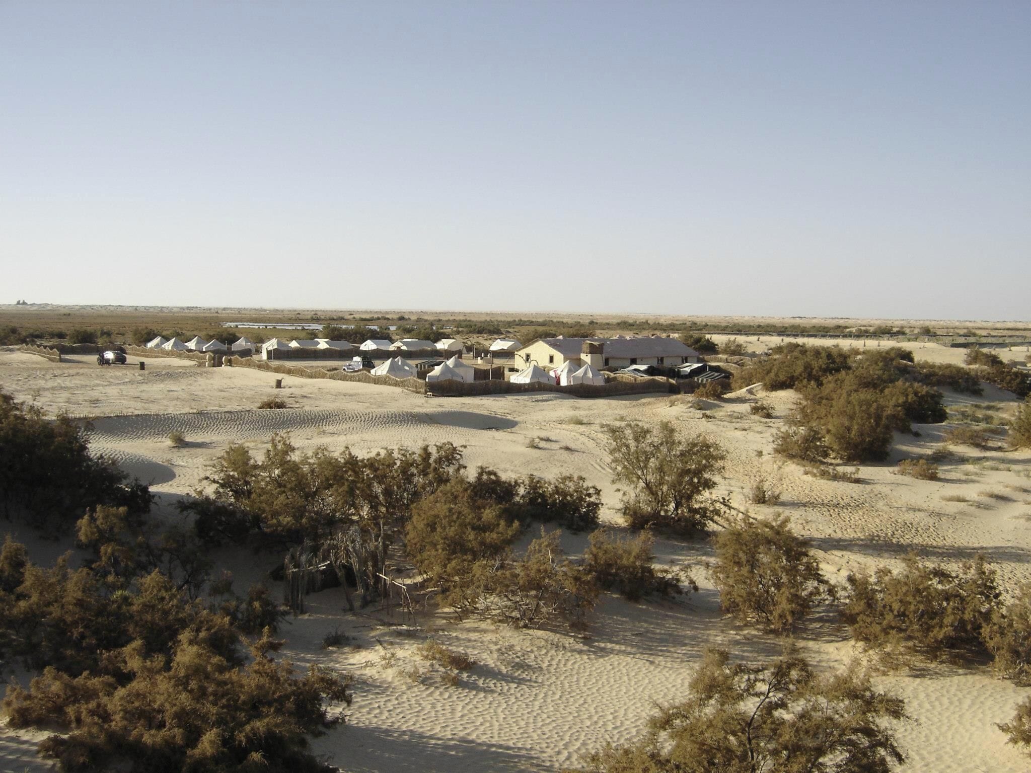 A desert landscape with multiple white tents and a few buildings.