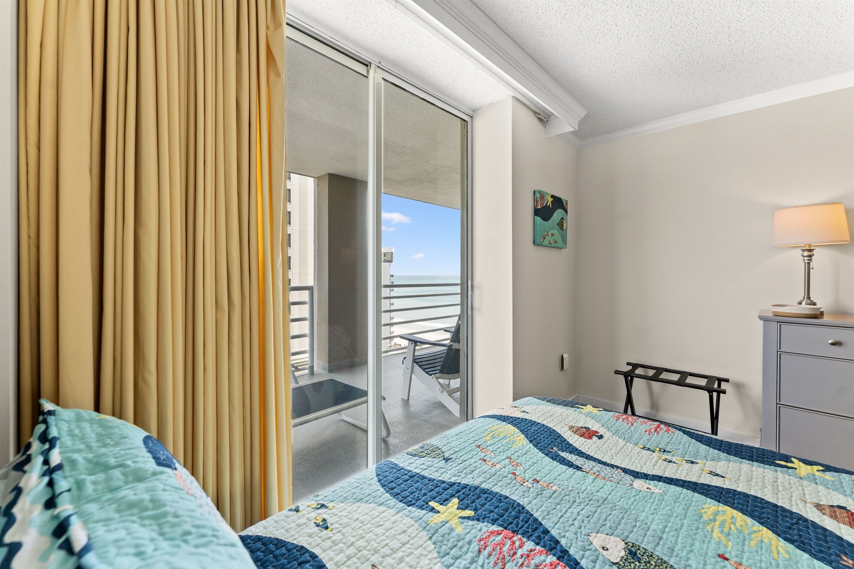 A hotel room with a bed, a view to the outside, a small table, and a lamp.