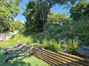 A garden with a pond, wooden fence, and lounge chairs.