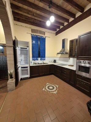 A kitchen with a built-in oven, a refrigerator, dark wooden cabinets, a tiled backsplash, and a patterned floor.