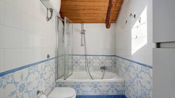 Een badkamer met douche, toilet en wastafel, voorzien van blauw-witte betegelde muren en houten balken in het plafond.
