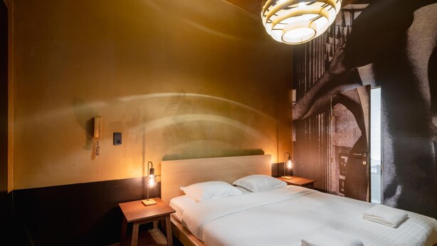 A hotel room with a bed, bedside tables, a wall-mounted phone, and a unique architectural feature. - 1-bedroom Apartment in National Residence (Antwerp)