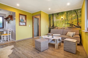Ein Wohnzimmer mit einer Couch, zwei Poufs, einem Tisch und einem Essbereich mit Stühlen.