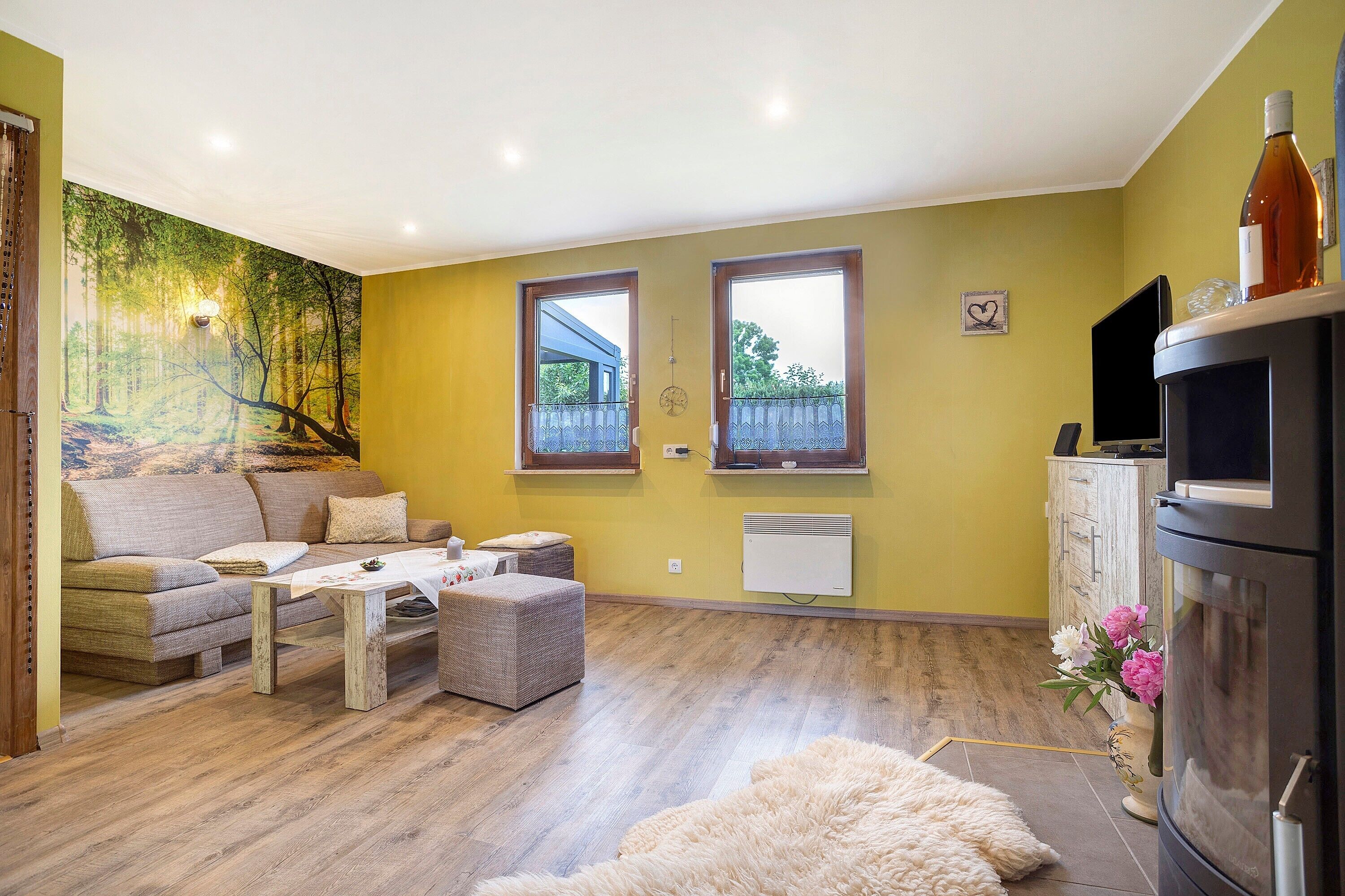 Een woonkamer met een bank, salontafel, poef, een open haard en een muurschildering.