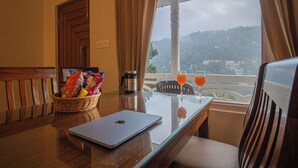 A room with a laptop, a basket of snacks, a coffee maker, and two glasses of orange juice on a table. - Alaya Stays Headingly Suite Lake Facing (Nainital)