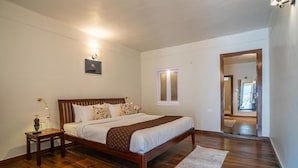 A bedroom with a wooden bed, a nightstand, a bedside table, a mirror, and a door leading to another room. - Alaya Stays Headingly Suite Lake Facing (Nainital)