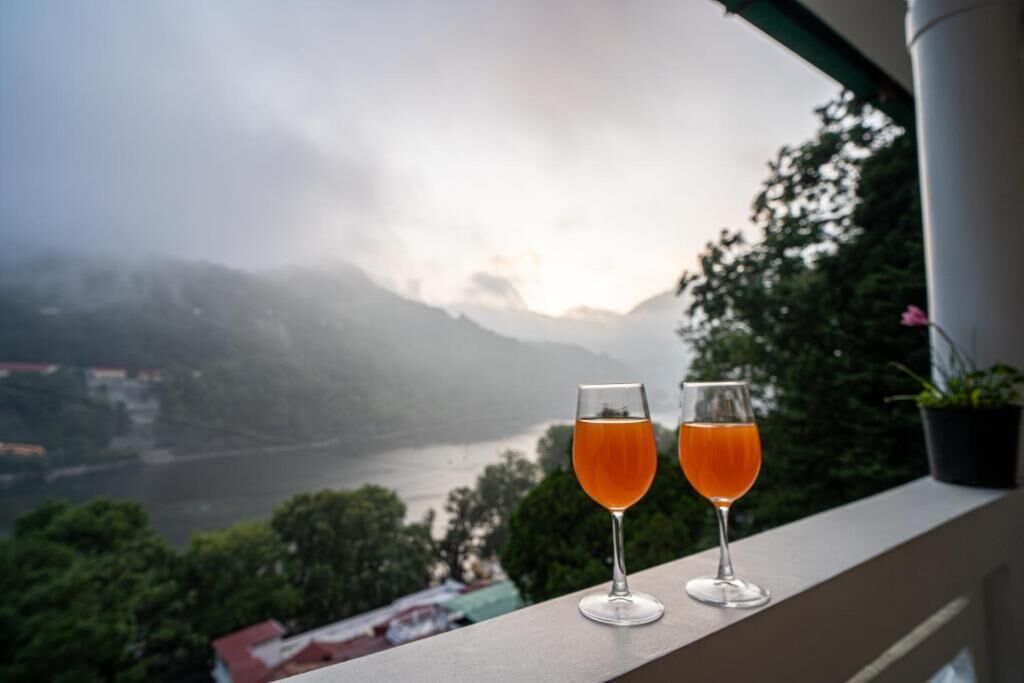 Zwei Gläser Orangensaft auf einem Balkon mit Blick auf einen Fluss und Berge.