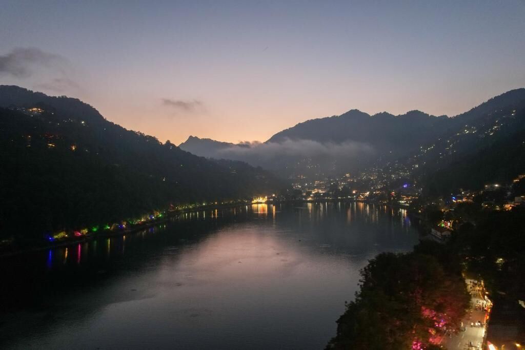 Vista nocturna de un lago con un puente y luces de una ciudad a lo lejos.