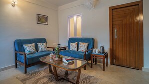 A living room with two blue sofas, a glass coffee table, a wooden side table, and a wooden door. - Alaya Stays Headingly Suite Lake Facing (Nainital)