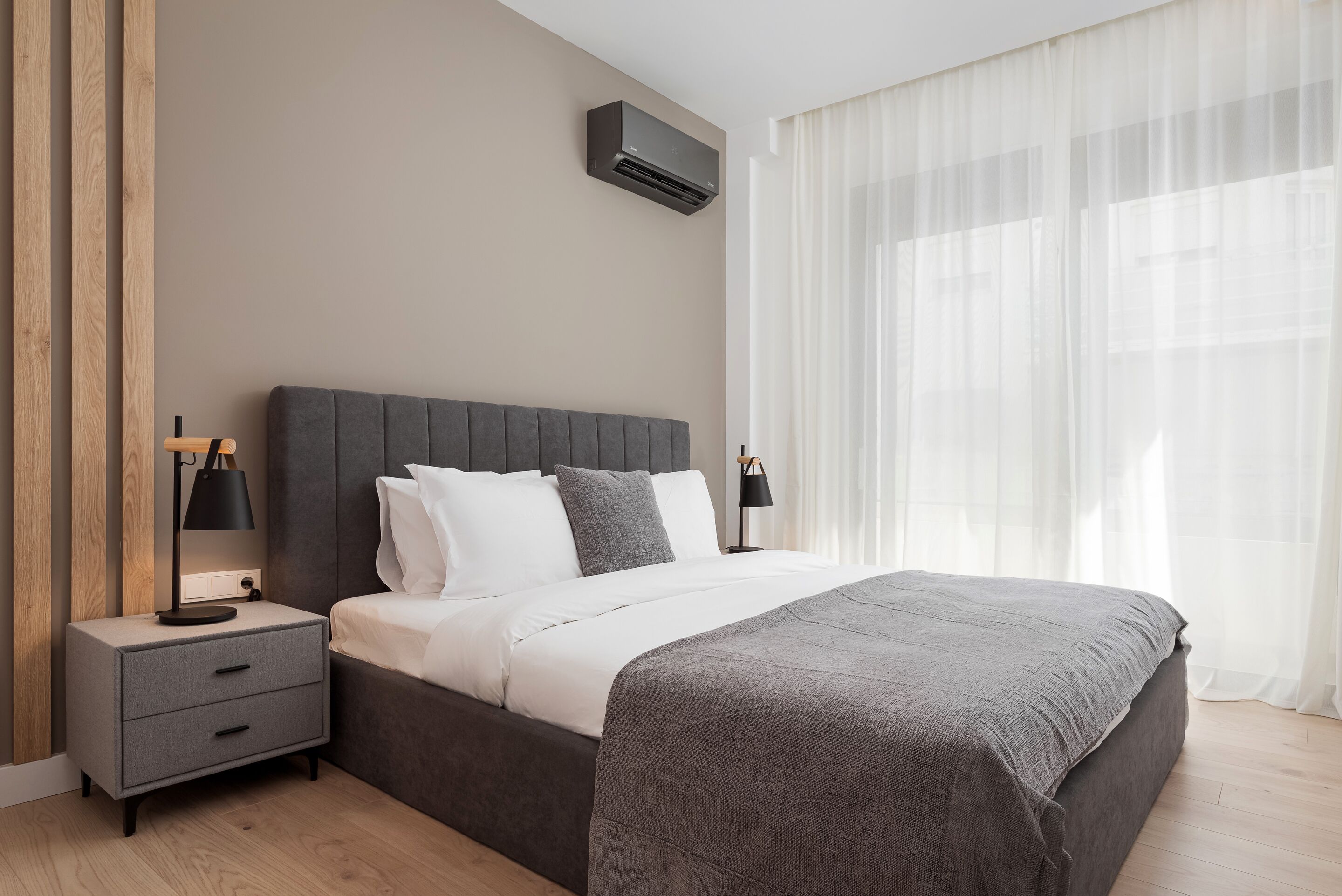 A modern bedroom with a bed, bedside tables, and an air conditioning unit.