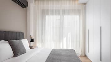 Une chambre à coucher moderne, avec un lit, une table de chevet, une lampe et une grande fenêtre ornée de rideaux légers.