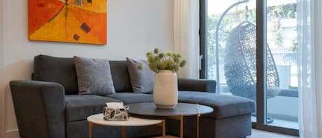 A modern living room with a grey sofa, a red rug, a white vase with greenery, and a large window with a view.