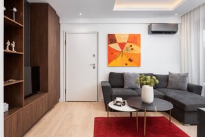 A modern living room with a sectional sofa, a flat-screen TV, a red rug, and a painting on the wall. - Alimos Escape 1 (Alimos)