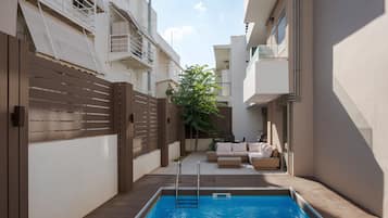 Une piscine avec une terrasse en bois, un espace délimité par une clôture et un coin salon agrémenté de coussins.