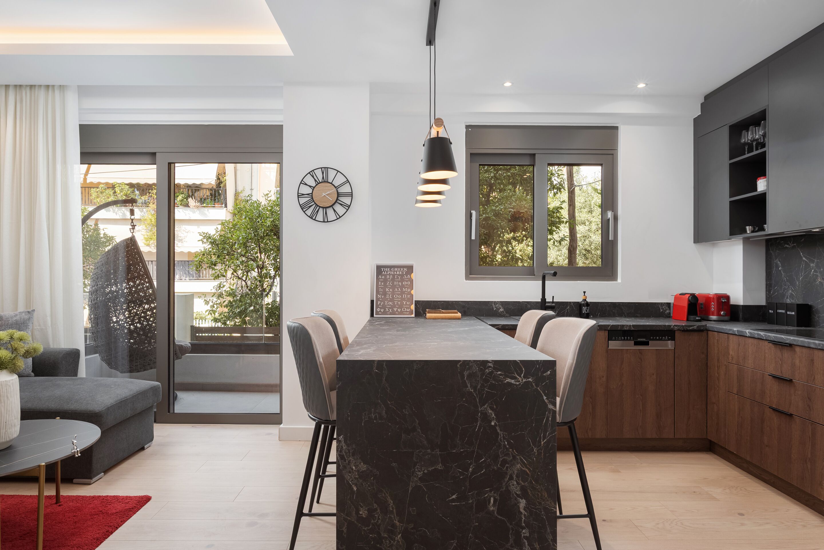 A modern kitchen with a marble island, dark cabinetry, and a built-in oven.