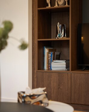 A wooden bookshelf with books and decorative items, a television on a stand, and a blurred object in the foreground. - Alimos Escape 1 (Alimos)