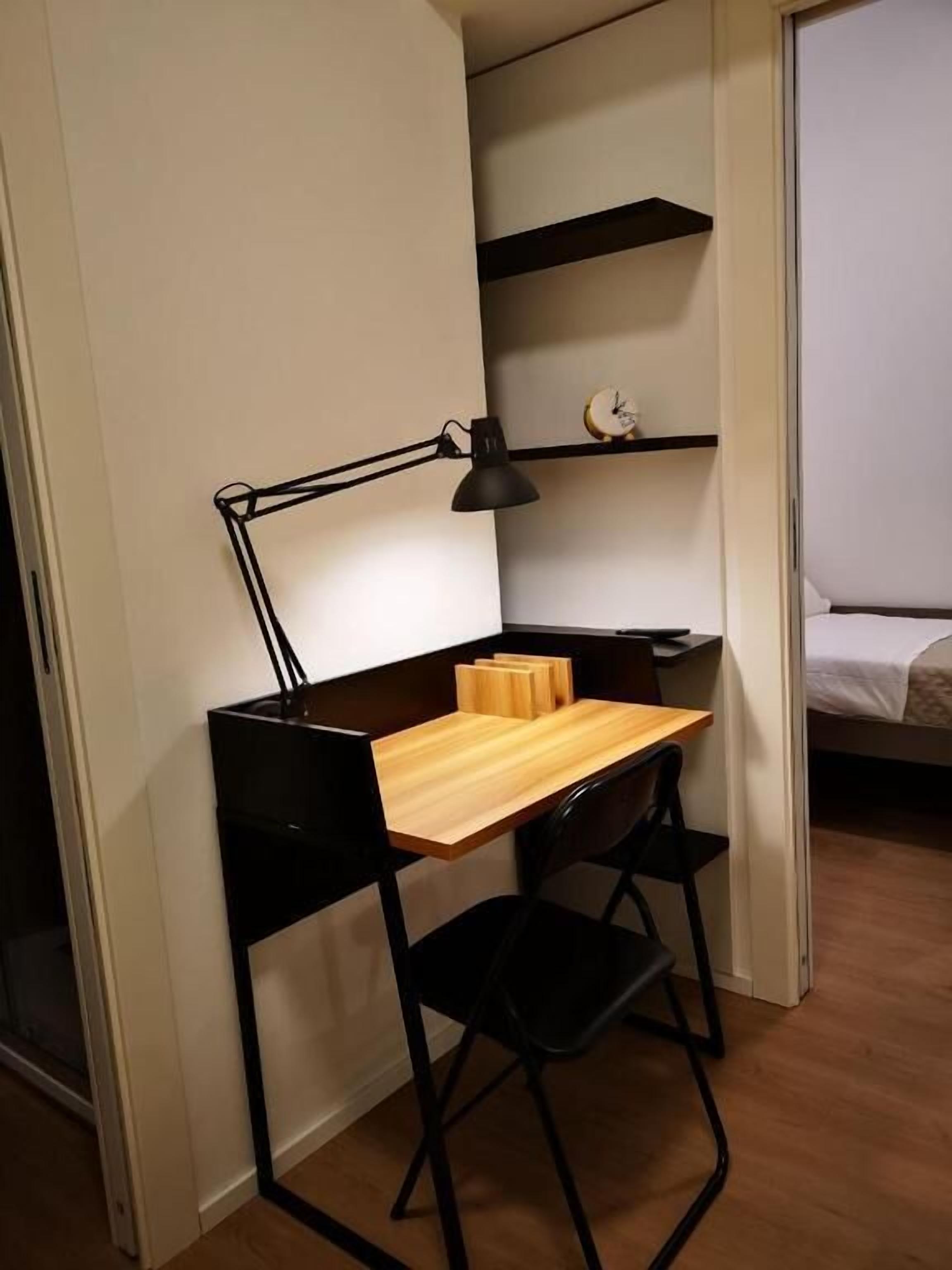 Un espacio de trabajo pequeño con un escritorio, una silla y una lámpara de escritorio negra.