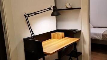 Un espacio de trabajo pequeño con un escritorio, una silla y una lámpara de escritorio negra.