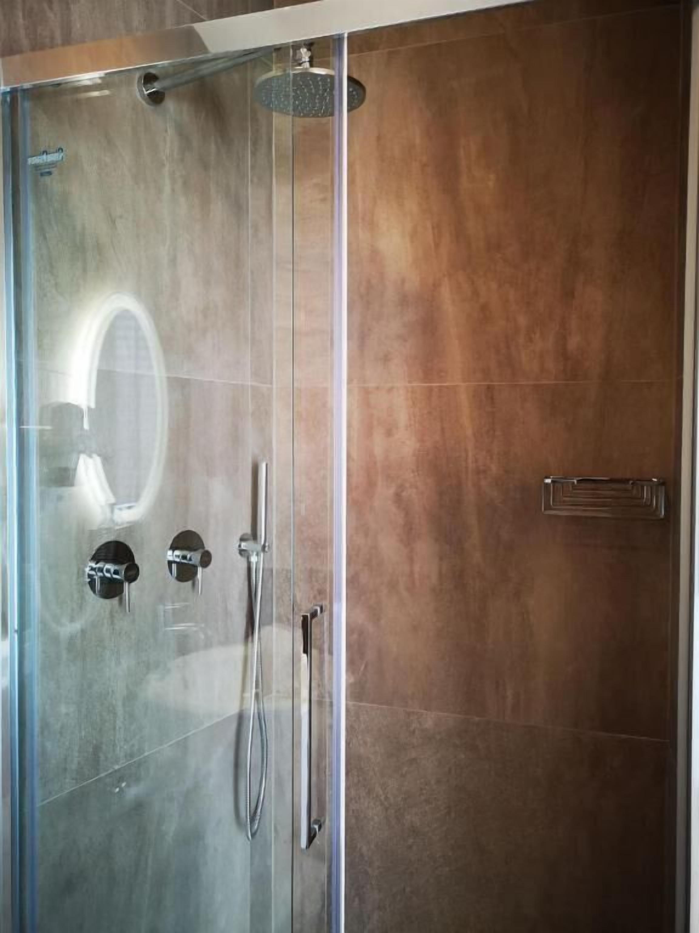 A glass-enclosed shower with a handheld showerhead and a wall-mounted faucet.