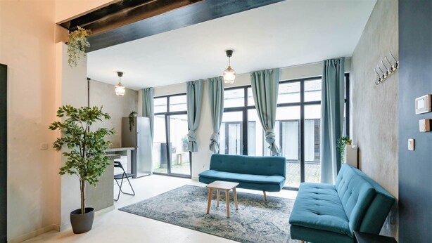 Una sala de estar con un sofá, una mesita, una planta en maceta y un ventanal con cortinas.