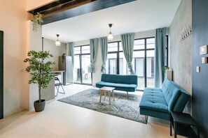 A living room with a sofa, a small table, a potted plant, and a large window with curtains. - Antwerp Central Superior Apartment (Antwerp)