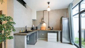 Una cocina moderna con lavavajillas integrado, extractor de acero inoxidable y un amplio ventanal con cortinas.
