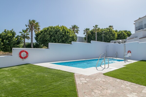 Une piscine équipée d’une bouée de sauvetage, un chemin de pierre et un mur blanc agrémenté d’un balcon.