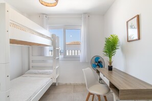 Une chambre avec un lit superposé, un bureau, une chaise et une plante en pot.