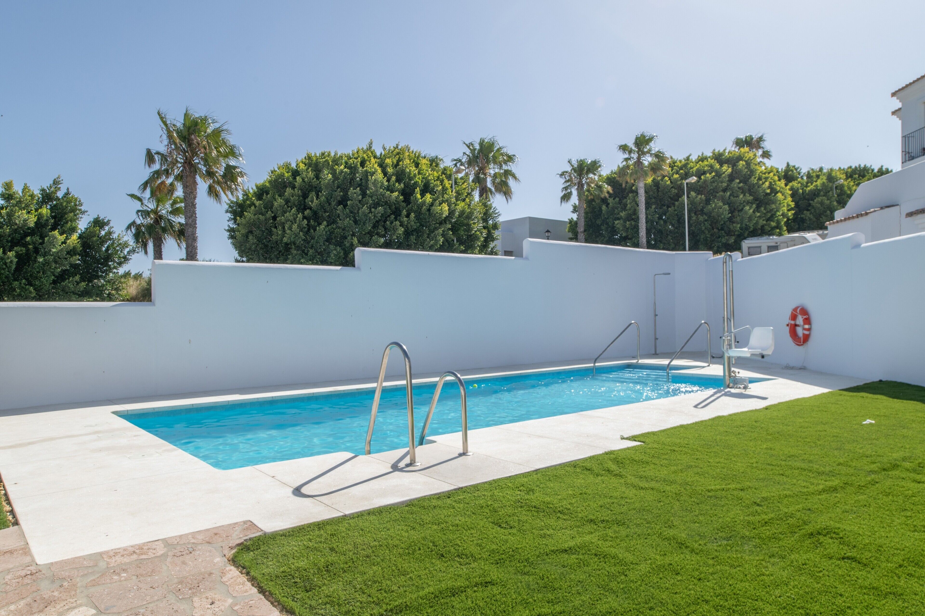 A swimming pool with steps, a lifebuoy, and a grassy area.