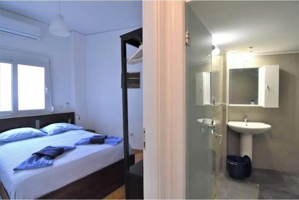 Ein Schlafzimmer mit Bett, Nachttisch, Fenster und einem Badezimmer mit Waschbecken und Spiegel.
