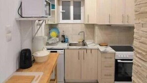 Une cuisine compacte avec des meubles de couleur claire, un four à micro-ondes, un évier, une cuisinière et une petite table à manger avec une planche à découper.