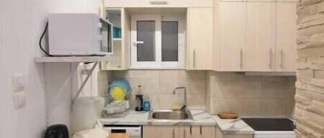 Une cuisine compacte avec des meubles de couleur claire, un four à micro-ondes, un évier, une cuisinière et une petite table à manger avec une planche à découper.