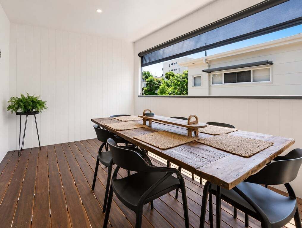 Un coin repas avec une table en bois, des chaises noires et une vue par la fenêtre.