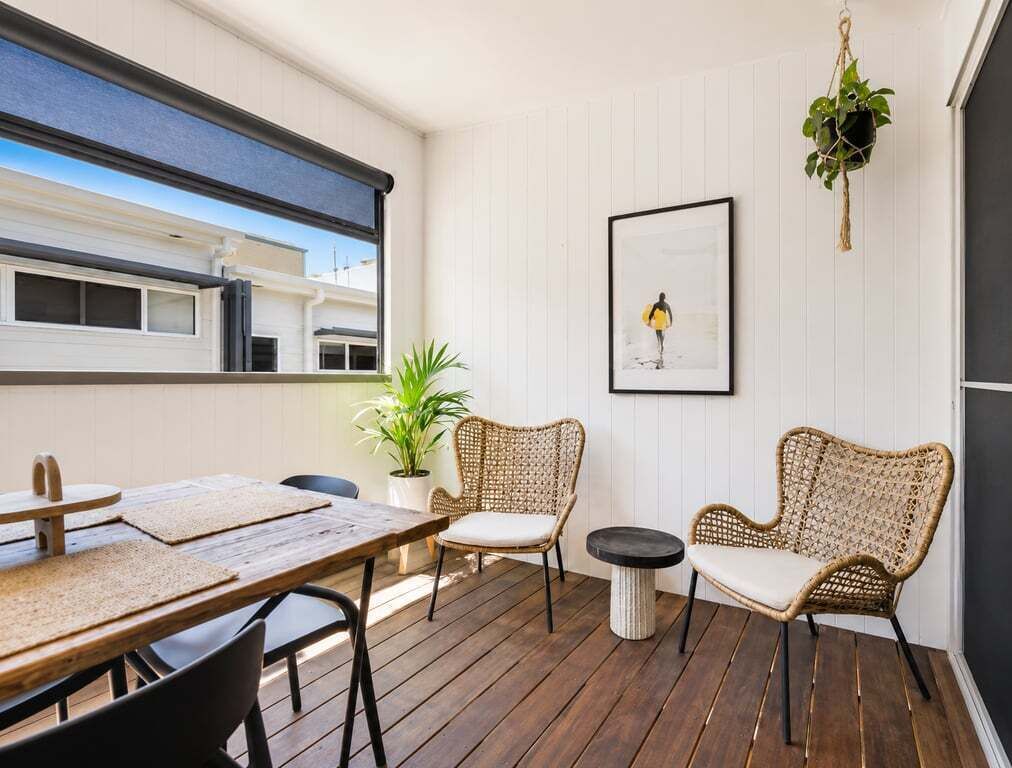 Ein Zimmer mit Holzterrasse, Korbmöbeln, einem gerahmten Bild und einer hängenden Pflanze.