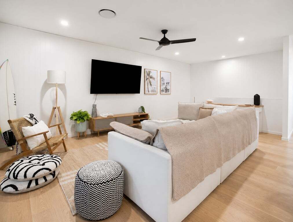 A modern living room with a white sofa, a flat-screen TV, a ceiling fan, and a wooden floor.