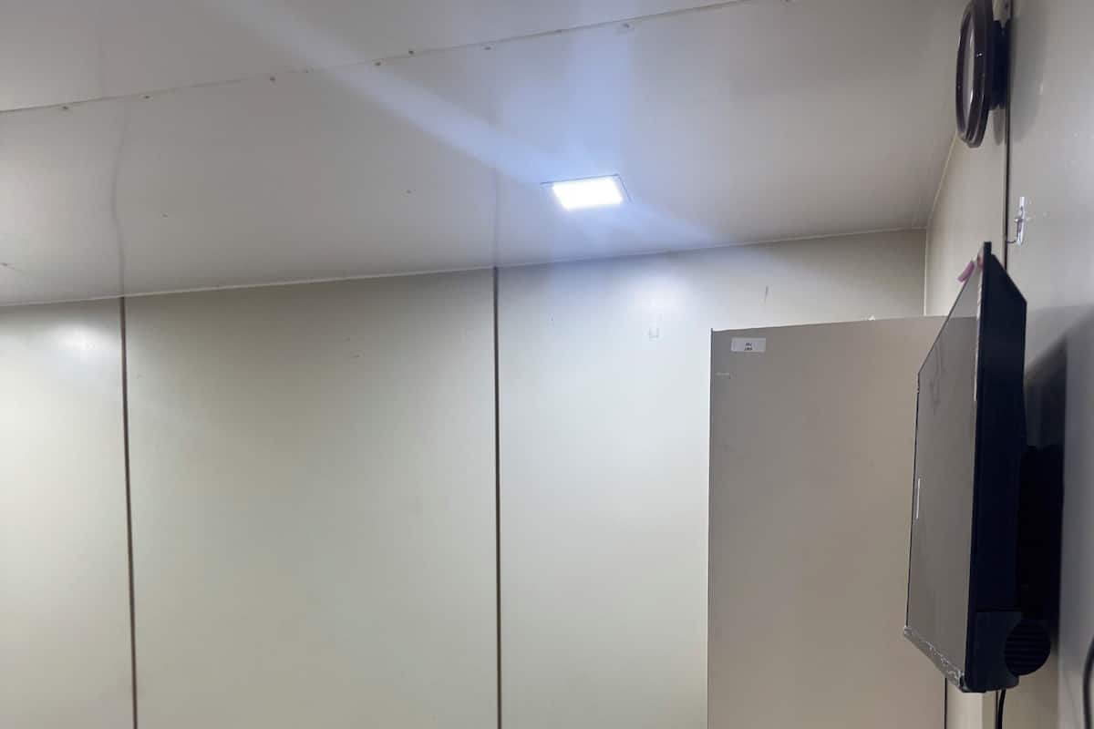 A room with a bed, a small white cabinet, a wall-mounted TV, and a ceiling light.