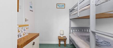 A bunk bed room with a wooden dresser, a small table with a lamp, and a framed picture on the wall.
