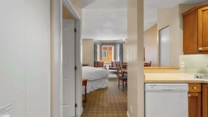 Ein Hotelzimmer mit Bett, Esstisch mit Stühlen, Küchenzeile inklusive Geschirrspüler und Blick ins Freie durch ein Fenster.