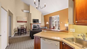 A compact kitchen with a dishwasher, a dining area with chairs, a television, and a view through a glass door.