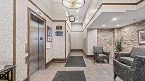 A hotel lobby with an elevator, a clock, a reception desk, and seating area.