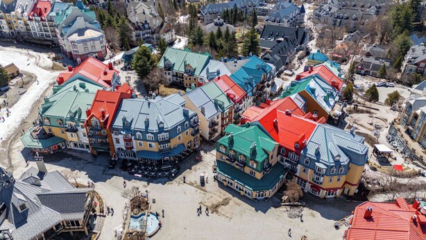 A cluster of colorful buildings with a central courtyard, surrounded by trees and a sandy area.