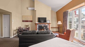 A hotel room with a fireplace, a television, a sofa, a bed, and a window with a view of buildings.