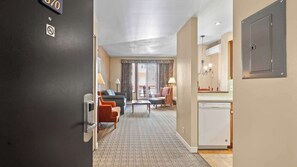 Ein Hotelzimmer mit einer Couch, Sesseln, einem Esstisch, einer Küchenzeile und einem Badezimmer.