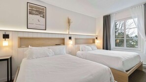 Ein Hotelzimmer mit zwei Betten, einem gerahmten Bild an der Wand und einem Fenster mit Vorhängen.
