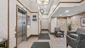 Eine Hotelhalle mit Aufzug, einer Uhr, einer Rezeption und einer Sitzecke.