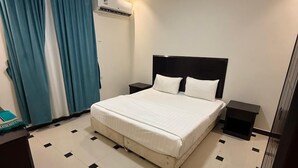 A hotel room with a bed, nightstands, an air conditioning unit, a blue curtain, and a tiled floor. - Quiet Rooms 13 (Riyadh)