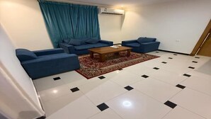 A living room with a sofa set, a coffee table, a red rug, and a tiled floor. - Quiet Rooms 13 (Riyadh)