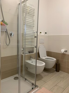 A bathroom with a glass-enclosed shower, a sink, two toilets, and a small shelf with toiletries. - HOUSE I.N. Apartment in the center of Sottomarina (Chioggia)